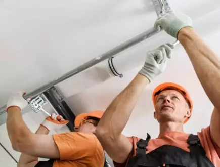 Two construction workers installing ceiling fixtures in a modern office building during daylight hours