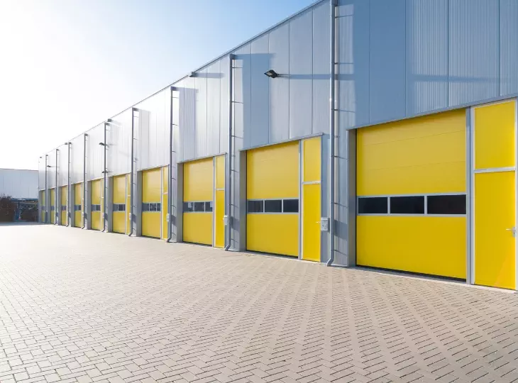 Modern industrial building with bright yellow loading doors and paved surface during sunny day