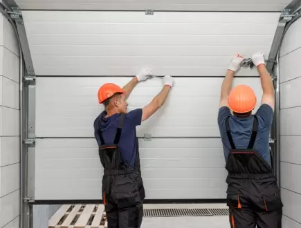Workers installing a garage door at a residential property in the afternoon with safety gear