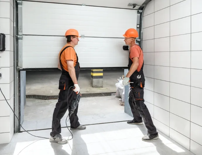 Two workers in safety helmets preparing to operate a garage door in a new building at a construction site Garage Door Installation