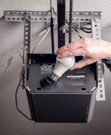 Hand adjusting light fixture with energy efficient bulb in home renovation project indoors Replacing batteries in your garage door opener for uninterrupted use.