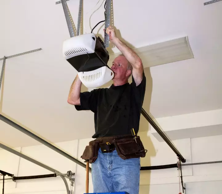 Man installs garage door opener while working on ceiling in residential garage Expert garage door opener repair service