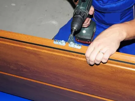 Worker assembles wooden furniture using power tools in a workshop during daylight hours