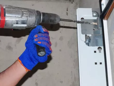 Man using a power drill to secure a metal bracket in place during home renovation project Repairing a broken garage door spring in a residential home