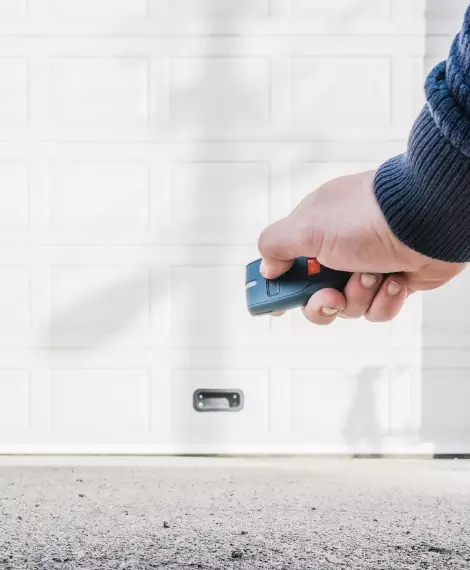 Hand holding remote control to open garage door at home on a sunny day Installing smart garage door openers for convenient control.